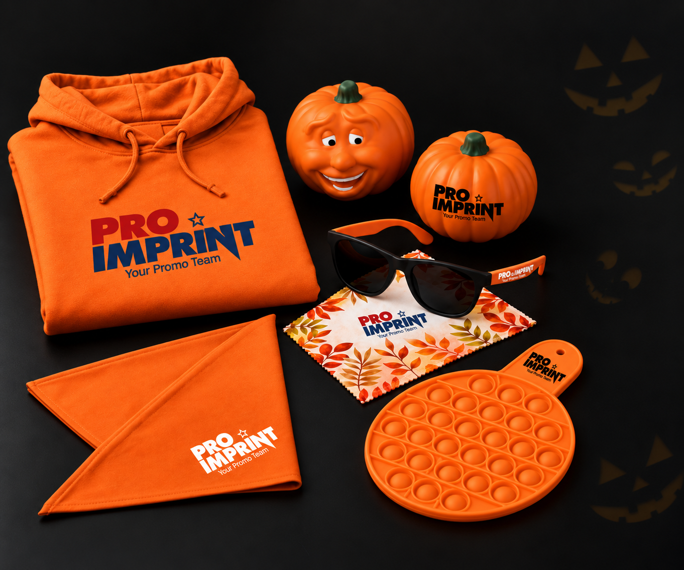 Orange Halloween-themed promotional products including a branded hoodie, pumpkin-shaped stress balls, custom sunglasses with microfiber cloth, a bandana, and a pop-it fidget toy, displayed on a black background with jack-o'-lantern accents.